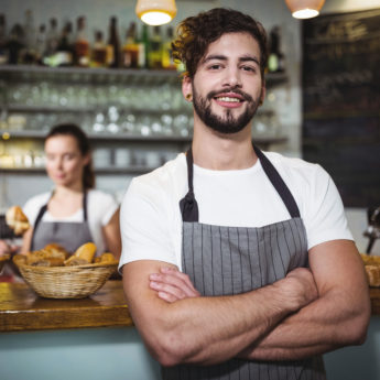 Smiling waiter standing with arms crossed in cafÃ©